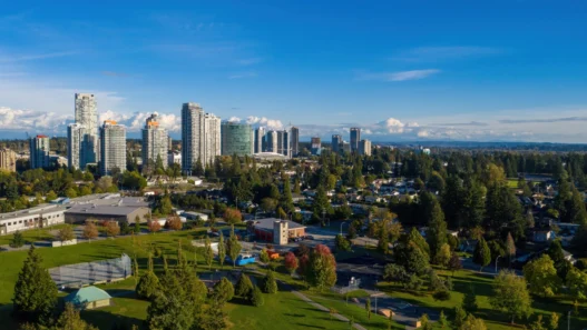 Surrey city skyline with high-rise buildings, green parks, and tree-lined neighborhoods under a bright blue summer sky.