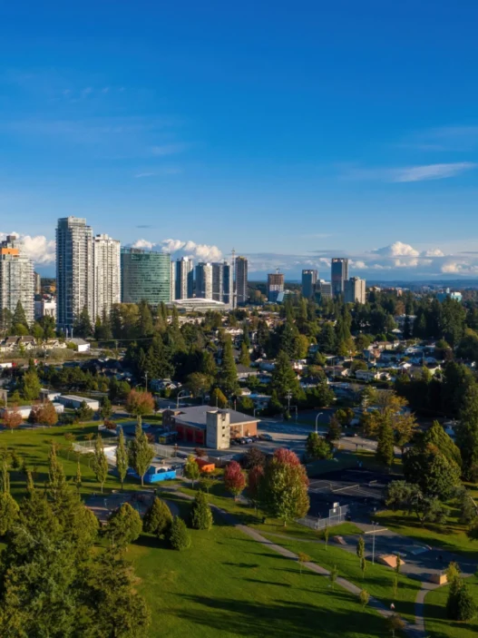 Surrey city skyline with high-rise buildings, green parks, and tree-lined neighborhoods under a bright blue summer sky.