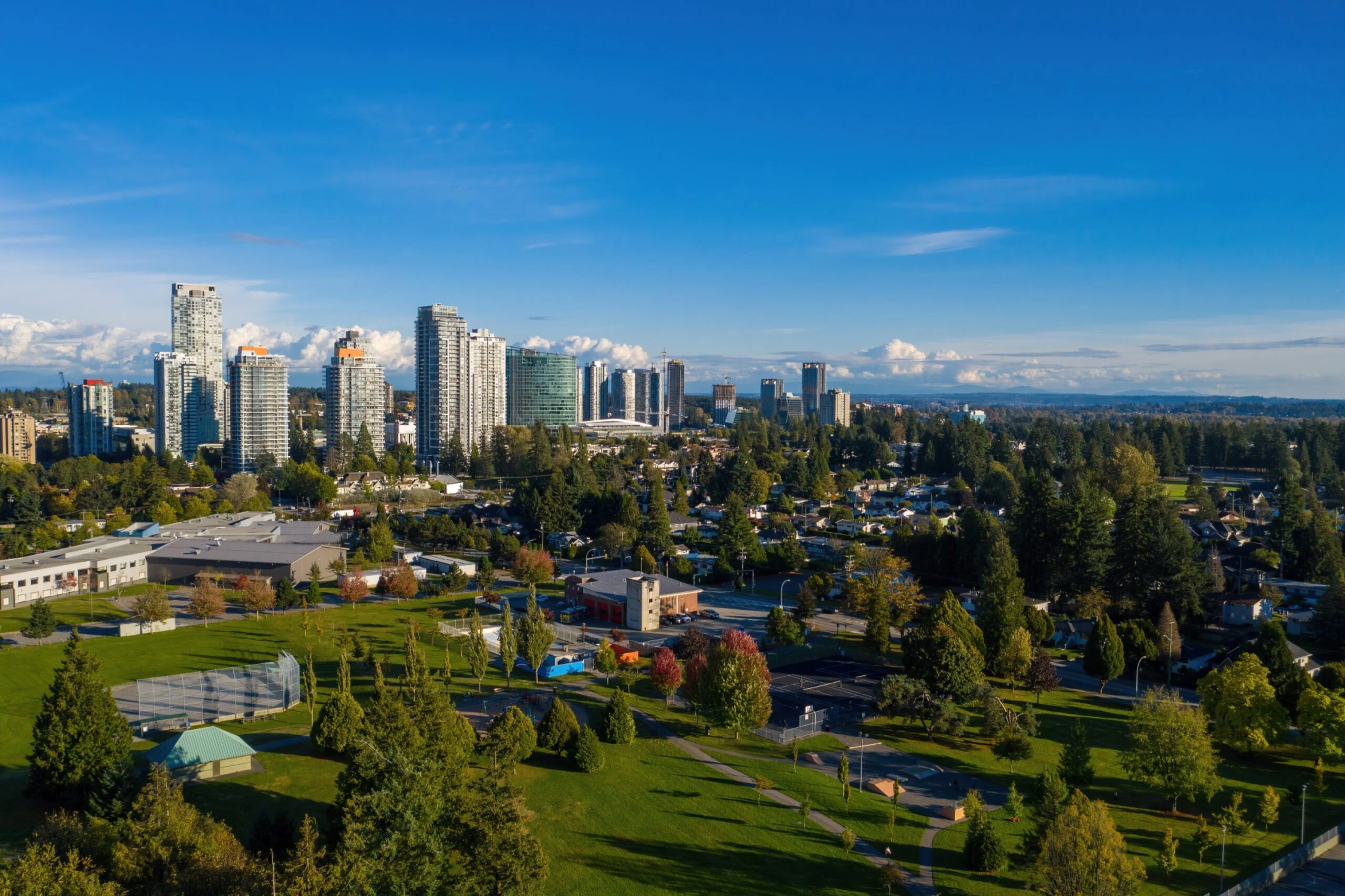 Surrey city skyline with high-rise buildings, green parks, and tree-lined neighborhoods under a bright blue summer sky.