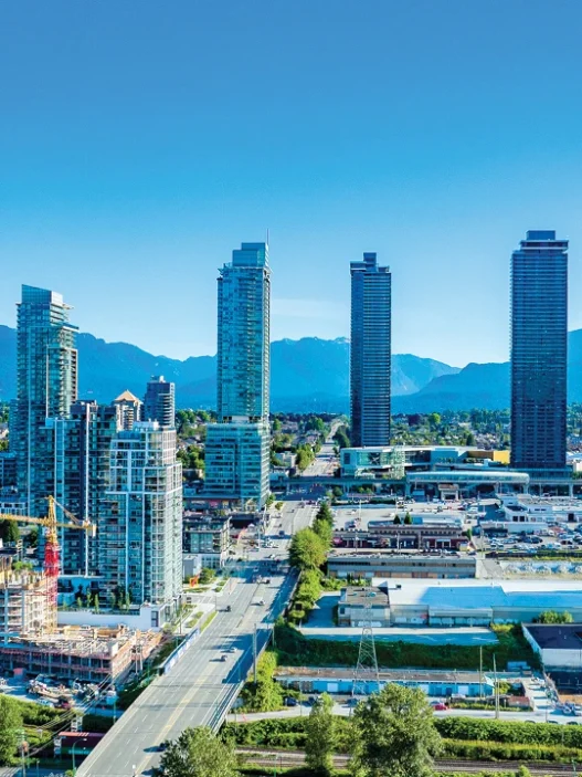 Burnaby city skyline with tall buildings, green spaces, and mountain views under a clear blue summer sky.