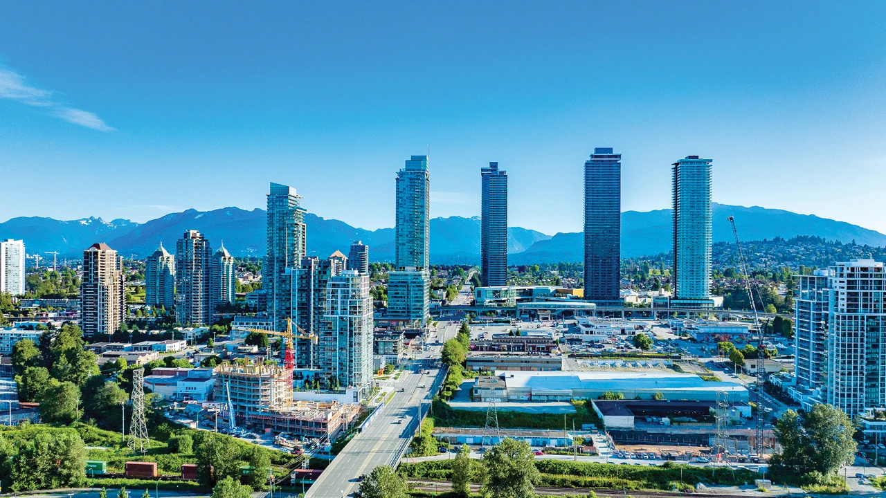 Burnaby city skyline with tall buildings, green spaces, and mountain views under a clear blue summer sky.