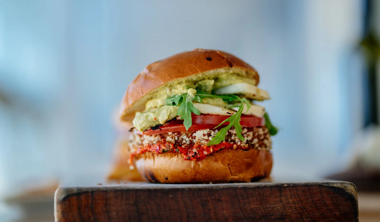 Gourmet quinoa burger from a vegan restaurant in Edmonton, stacked with avocado and fresh veggies.