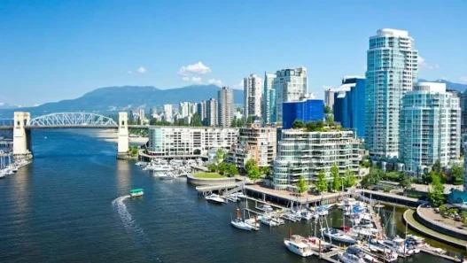 Vancouver waterfront shines in summer with yachts, sleek towers, and Burrard Bridge beneath a clear blue sky.