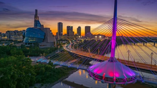 Sunset over Winnipeg with Esplanade Riel glowing in vibrant colors beside the city skyline.