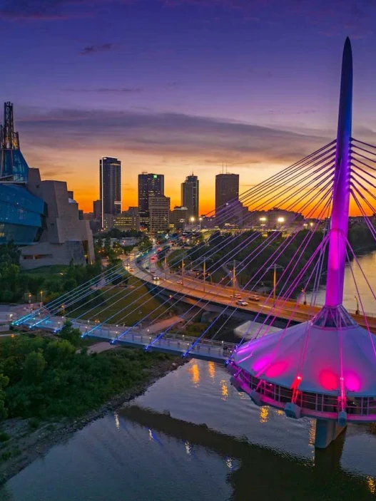 Sunset over Winnipeg with Esplanade Riel glowing in vibrant colors beside the city skyline.