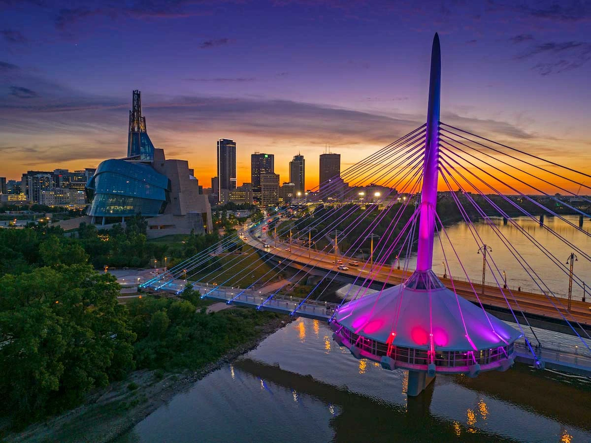 Sunset over Winnipeg with Esplanade Riel glowing in vibrant colors beside the city skyline.